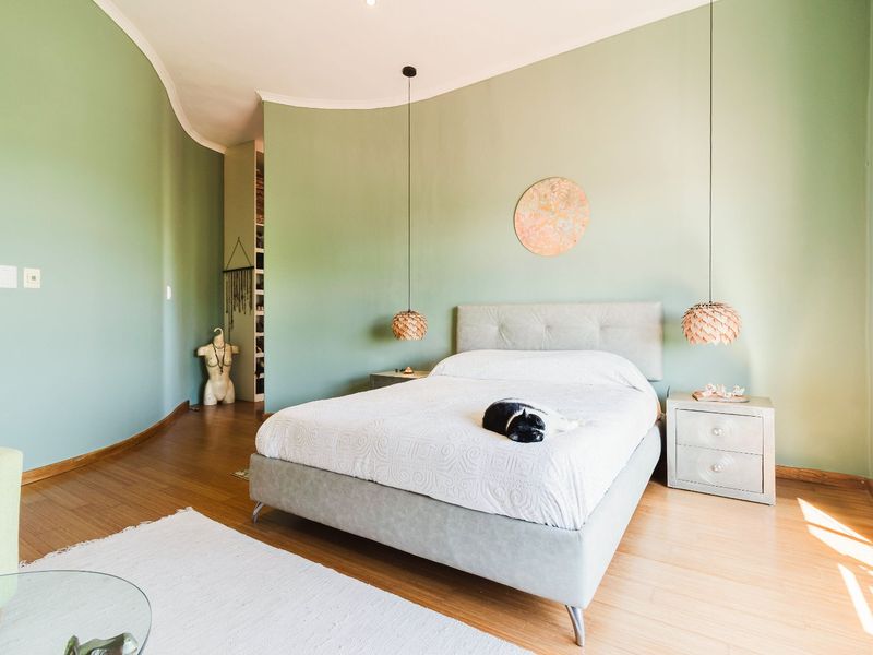 A spacious bedroom featuring hardwood flooring, a unique curved wall design, and built-in closet storage with modern pendant lighting.