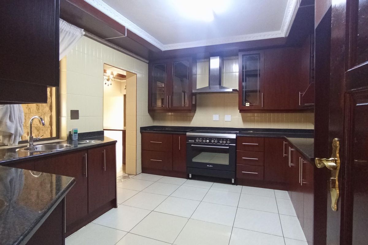 A functional kitchen featuring dark wood cabinetry, granite countertops, a stainless steel extractor fan, and a built-in oven with a gas hob.