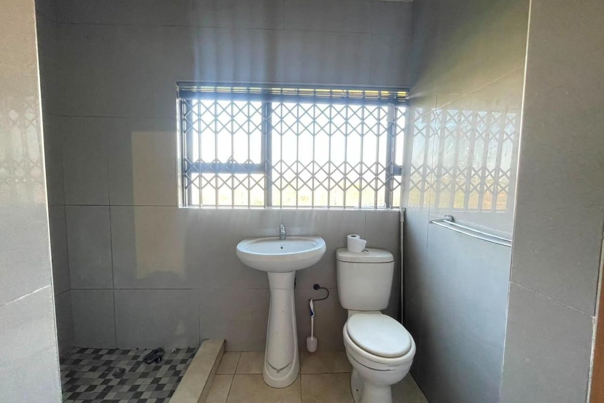 A functional bathroom featuring a pedestal basin, toilet, and tiled finishes, equipped with a security gate on the window.