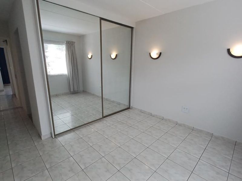 A bright, empty bedroom featuring tiled flooring, built-in mirrored wardrobes, and wall-mounted lighting fixtures.