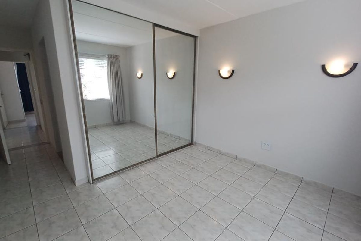 A bright, empty bedroom featuring tiled flooring, built-in mirrored wardrobes, and wall-mounted lighting fixtures.
