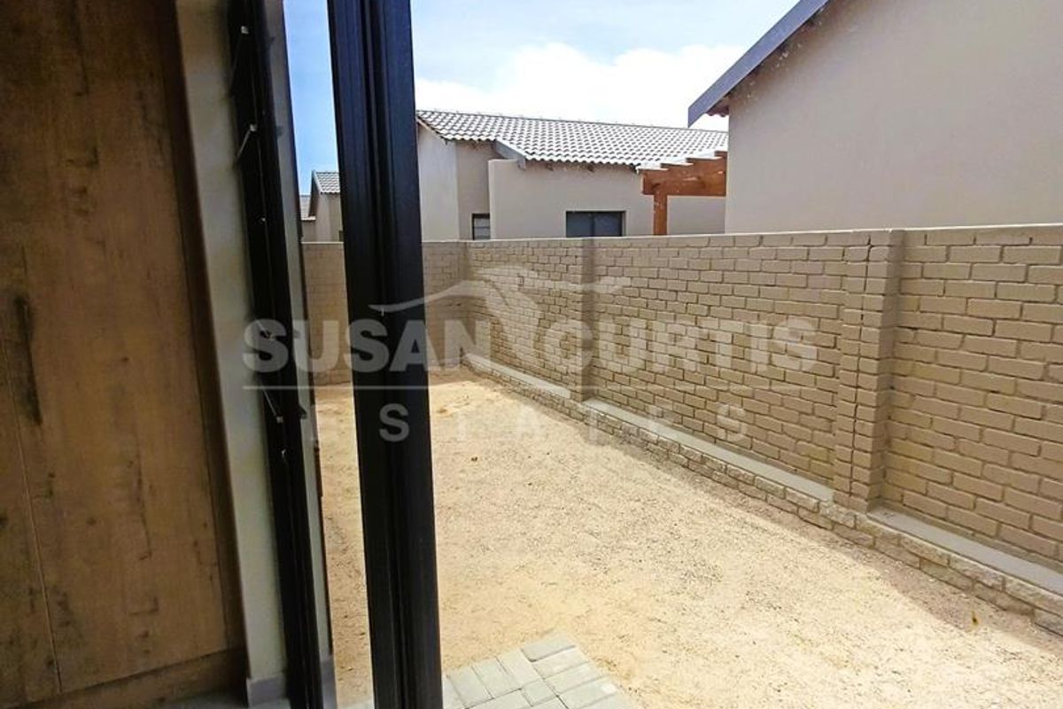 A view from the interior looking out onto a private rear courtyard featuring a paved patio area and perimeter brick walling.