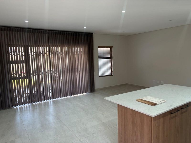 Spacious open-plan living area featuring a modern kitchen island with stone countertop, neutral tiled flooring, and large sliding doors with integrated security gates.