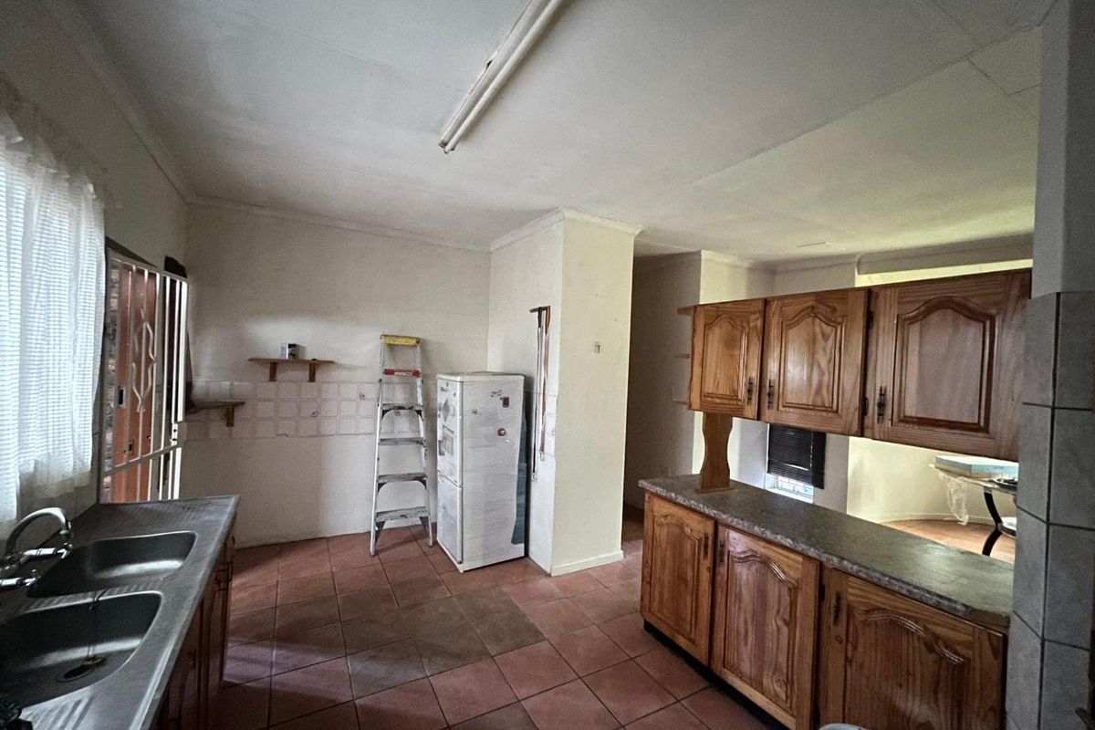 A dated kitchen featuring wooden cabinetry, a double basin sink, and tiled flooring, offering significant potential for renovation and modernization.