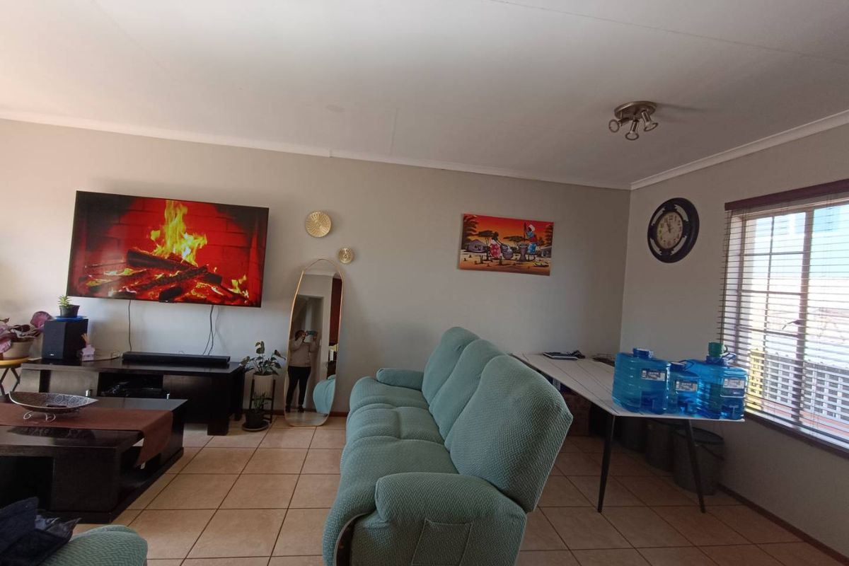 A living room featuring tiled flooring and a window with security bars, providing a functional and comfortable space for relaxation.