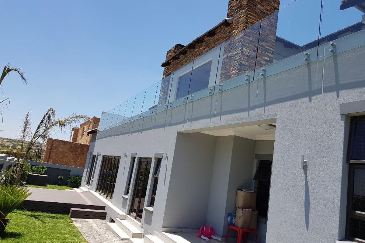 Rear view of the property featuring a modern glass balustrade balcony, stone-clad chimney stack, and a paved patio area overlooking the garden.