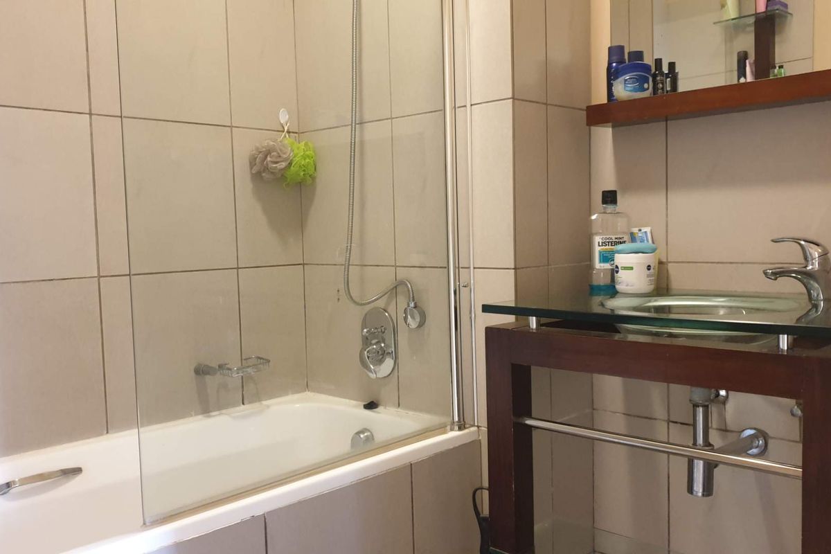 A functional bathroom featuring a bathtub with a glass shower screen, wall-mounted shower mixer, and a modern glass-top vanity unit.