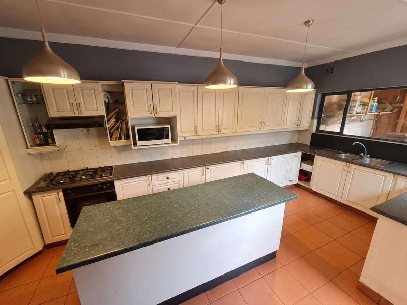 A functional kitchen featuring ample built-in cabinetry, a central island, gas hob, and integrated appliances, finished with tiled flooring and modern pendant lighting.