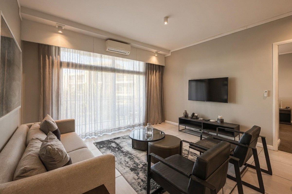A well-maintained living room featuring tiled flooring, a wall-mounted air conditioning unit, and large sliding glass doors providing access to the balcony.