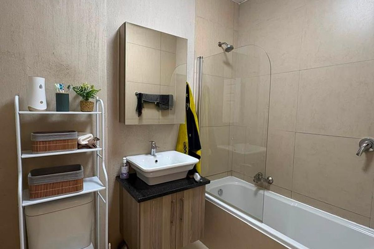 A functional bathroom featuring a vessel sink with vanity, a bathtub with a glass shower screen, and neutral wall and floor tiling.