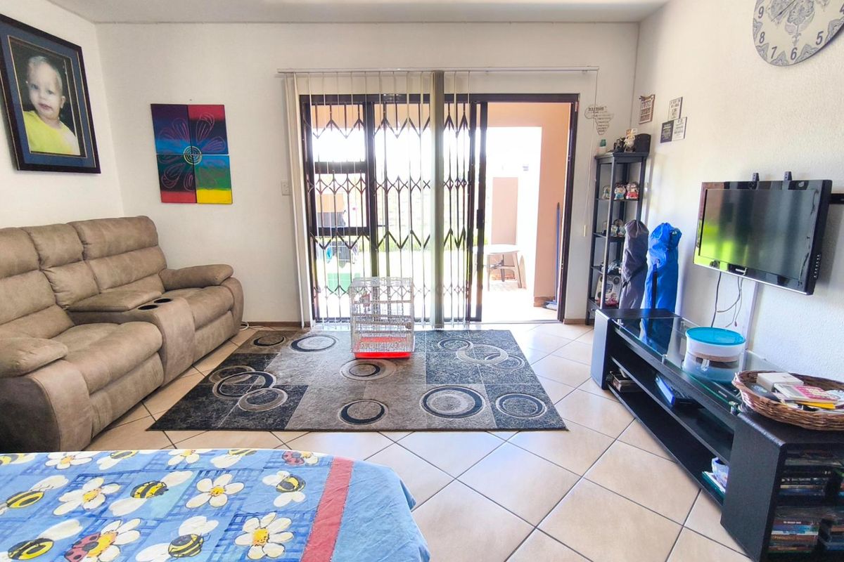 A comfortable living room featuring tiled flooring and sliding glass doors with security gates, providing direct access to an outdoor patio area.