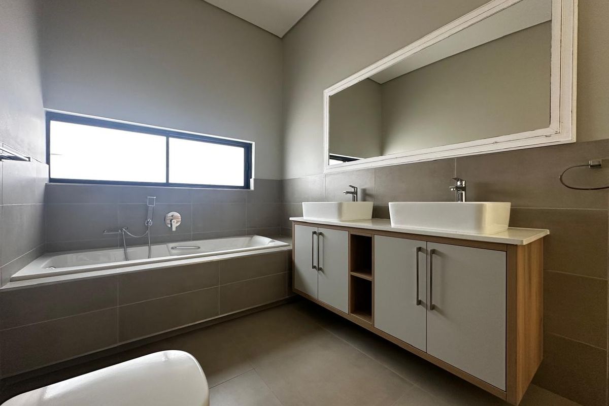 Modern bathroom featuring a double vanity with vessel sinks, a built-in bathtub, and large wall-mounted mirror with neutral tiling.
