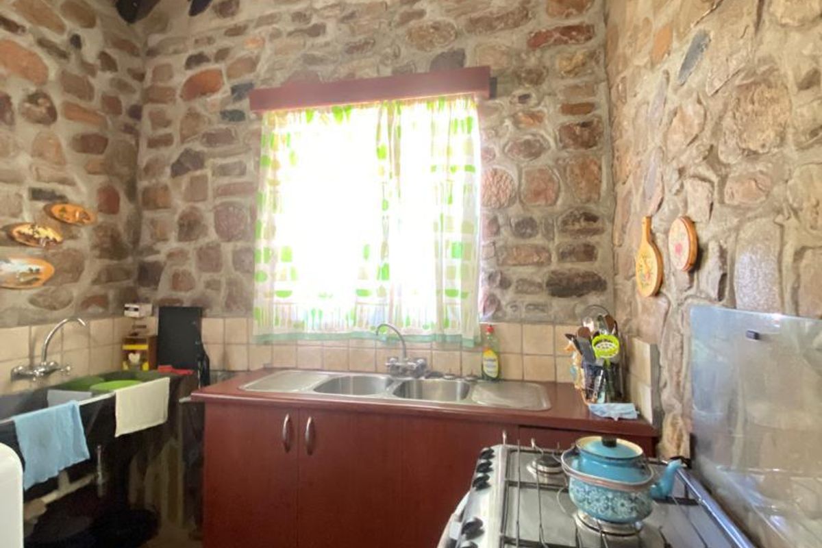 Rustic kitchen featuring exposed stone walls, a traditional thatched roof, built-in cabinetry, a double sink, and a gas stove.