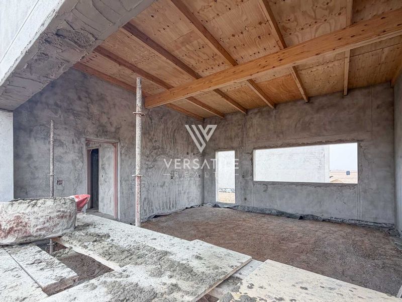 An unfinished open-plan living space currently under construction, featuring exposed timber ceiling beams, raw cement walls, and open window apertures.