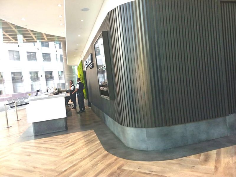 Modern office reception area featuring a curved dark slatted feature wall, herringbone flooring, and a sleek reception desk with floor-to-ceiling glass windows.