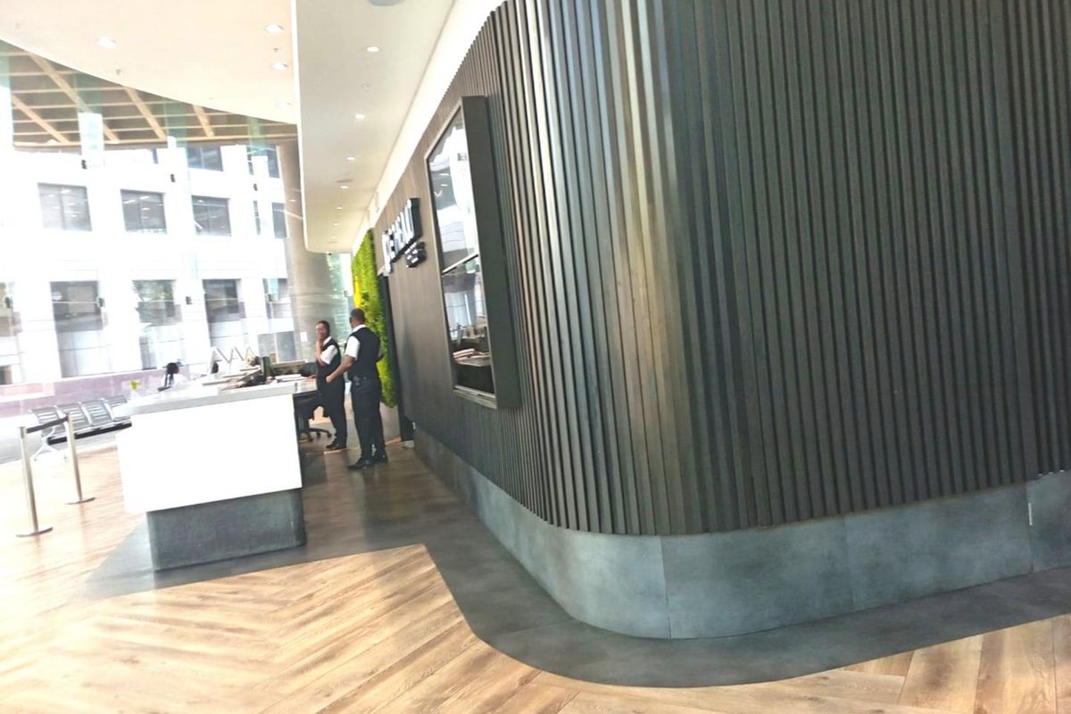 Modern office reception area featuring a curved dark slatted feature wall, herringbone flooring, and a sleek reception desk with floor-to-ceiling glass windows.