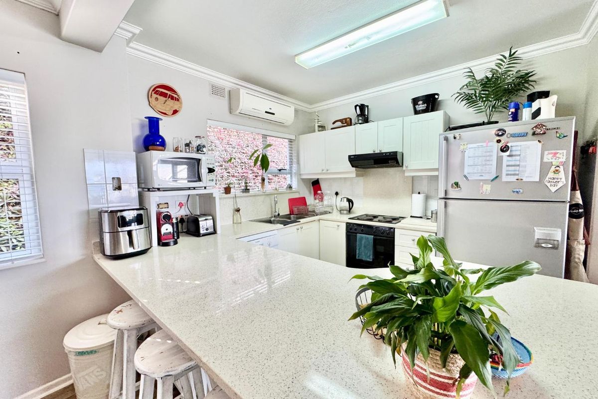 A functional kitchen featuring light-toned cabinetry, stone-look countertops, a breakfast bar, and integrated appliances including a hob and extractor fan.