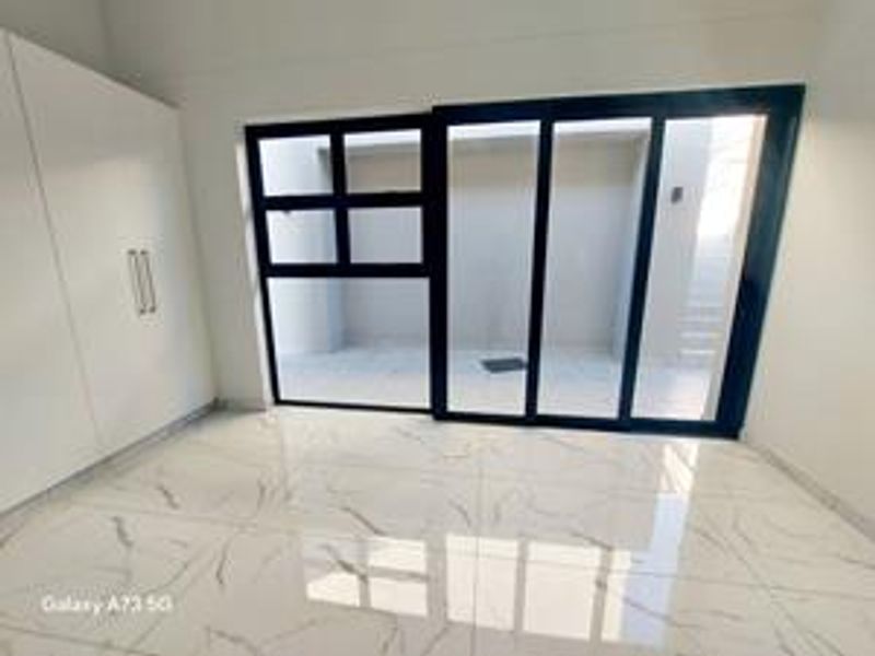 Bright living area featuring modern white built-in cupboards, large sliding glass doors leading to an outdoor space, and polished marble-look floor tiles.