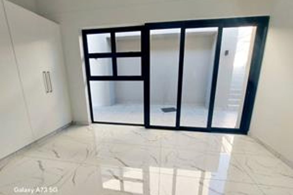 Bright living area featuring modern white built-in cupboards, large sliding glass doors leading to an outdoor space, and polished marble-look floor tiles.
