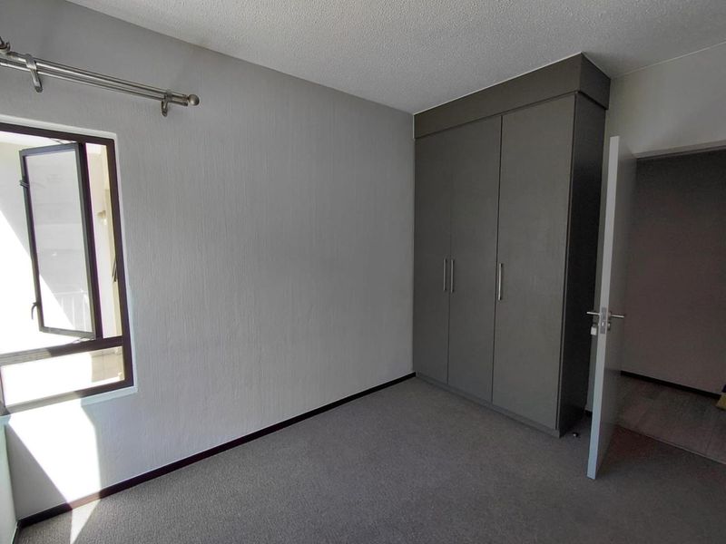 A clean, empty bedroom featuring neutral grey walls, carpeted flooring, and a built-in wardrobe with modern dark grey cabinetry.
