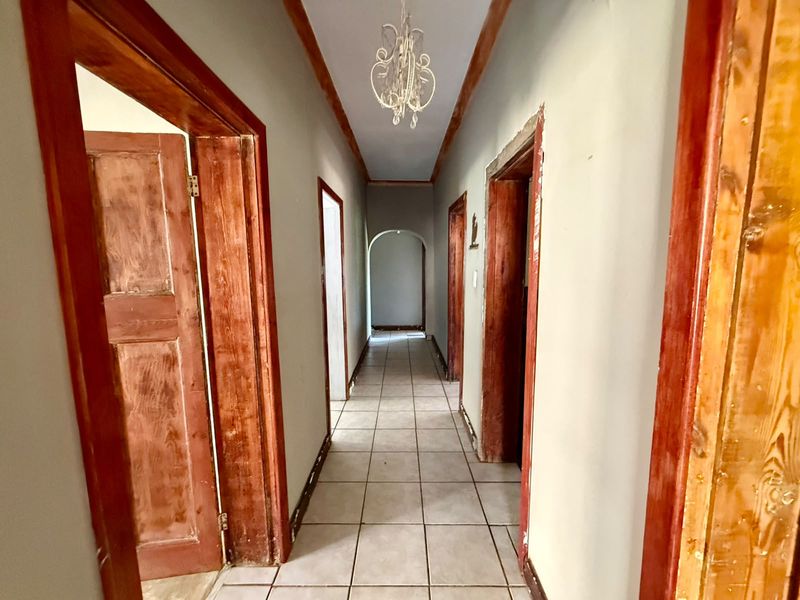 A long interior hallway featuring tiled flooring, multiple wooden door frames, and an arched transition, currently in need of cosmetic finishing and maintenance.