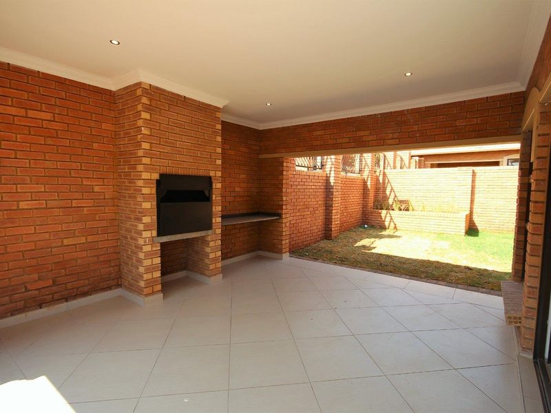 Covered patio area featuring a built-in brick braai, tiled flooring, and recessed lighting, overlooking a private garden space.