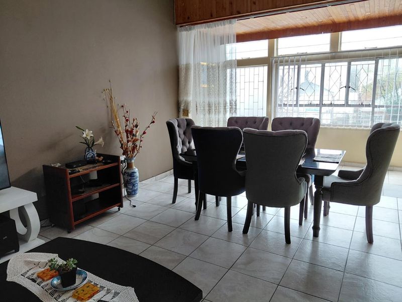 A dining area featuring tiled flooring, large windows with security bars, and timber ceiling paneling, providing a functional space for family meals.