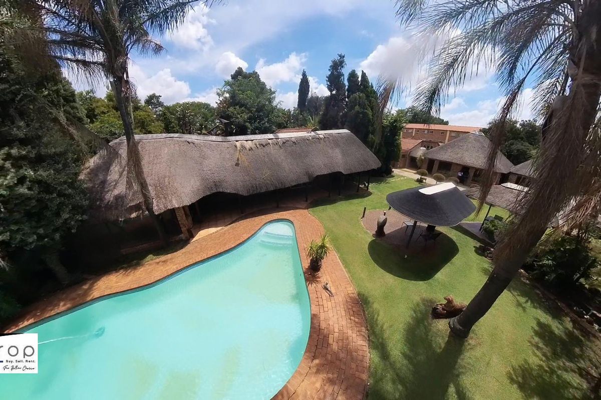 Aerial view of the guest house grounds featuring a swimming pool, expansive lawn, and traditional thatched roof structures.