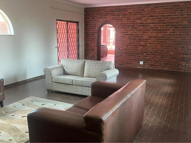 Spacious living area featuring a rustic exposed brick feature wall, arched doorway, and durable tiled flooring with access to an outdoor area.