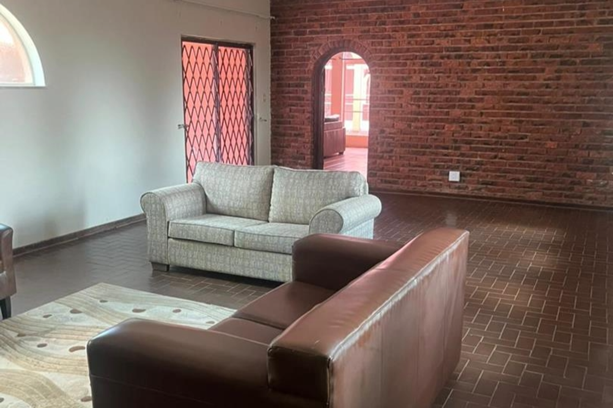 Spacious living area featuring a rustic exposed brick feature wall, arched doorway, and durable tiled flooring with access to an outdoor area.