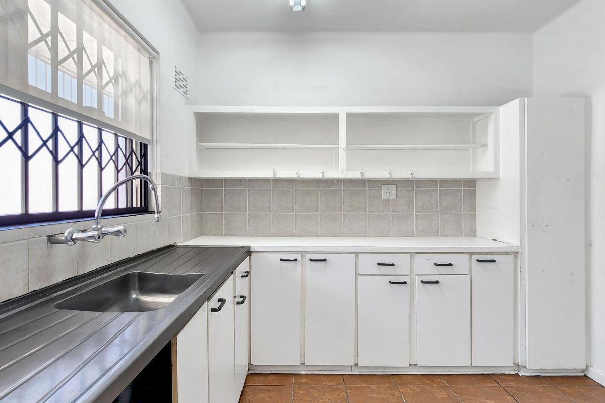 A functional kitchen featuring built-in white cabinetry, open shelving, a stainless steel sink, and tiled backsplash, offering a clean canvas for potential updates.