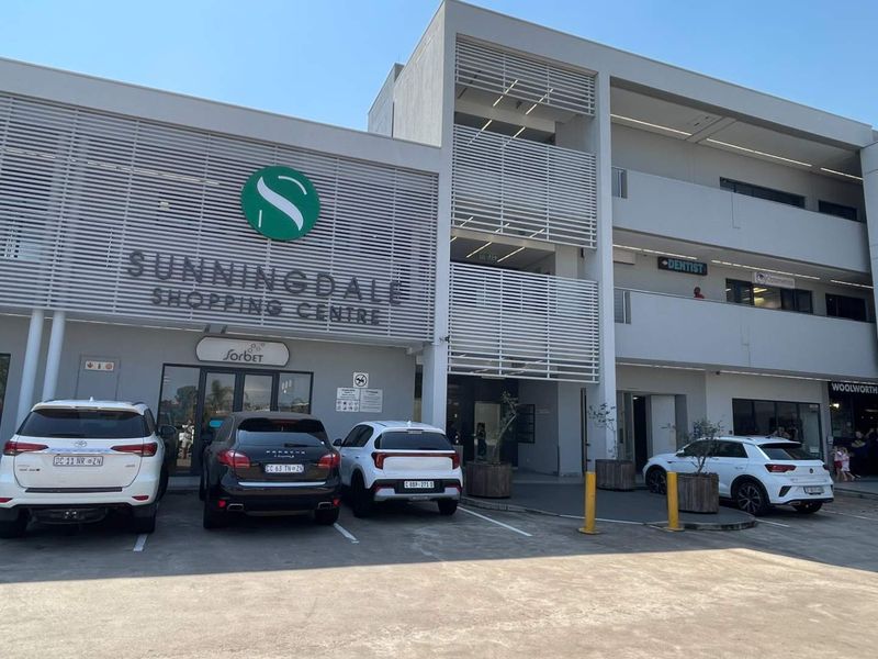 Front elevation of Sunningdale Shopping Centre featuring modern architectural louvre screening, paved parking area, and multi-level retail storefronts.