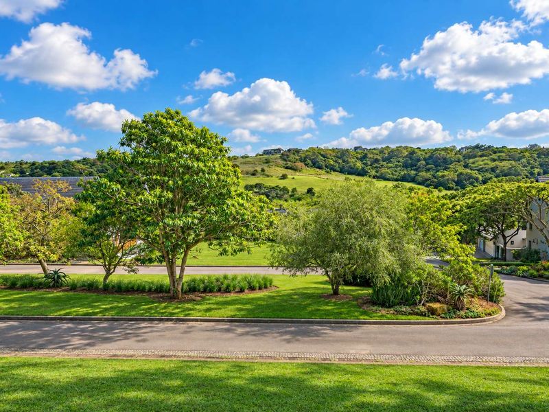 A scenic view of the surrounding landscape, featuring well-maintained green spaces, mature trees, and paved estate roads.