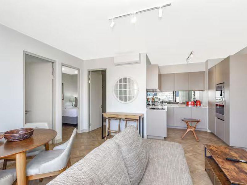 Modern open-plan living area featuring herringbone timber flooring, sleek built-in kitchen cabinetry with integrated appliances, and split-system air conditioning.