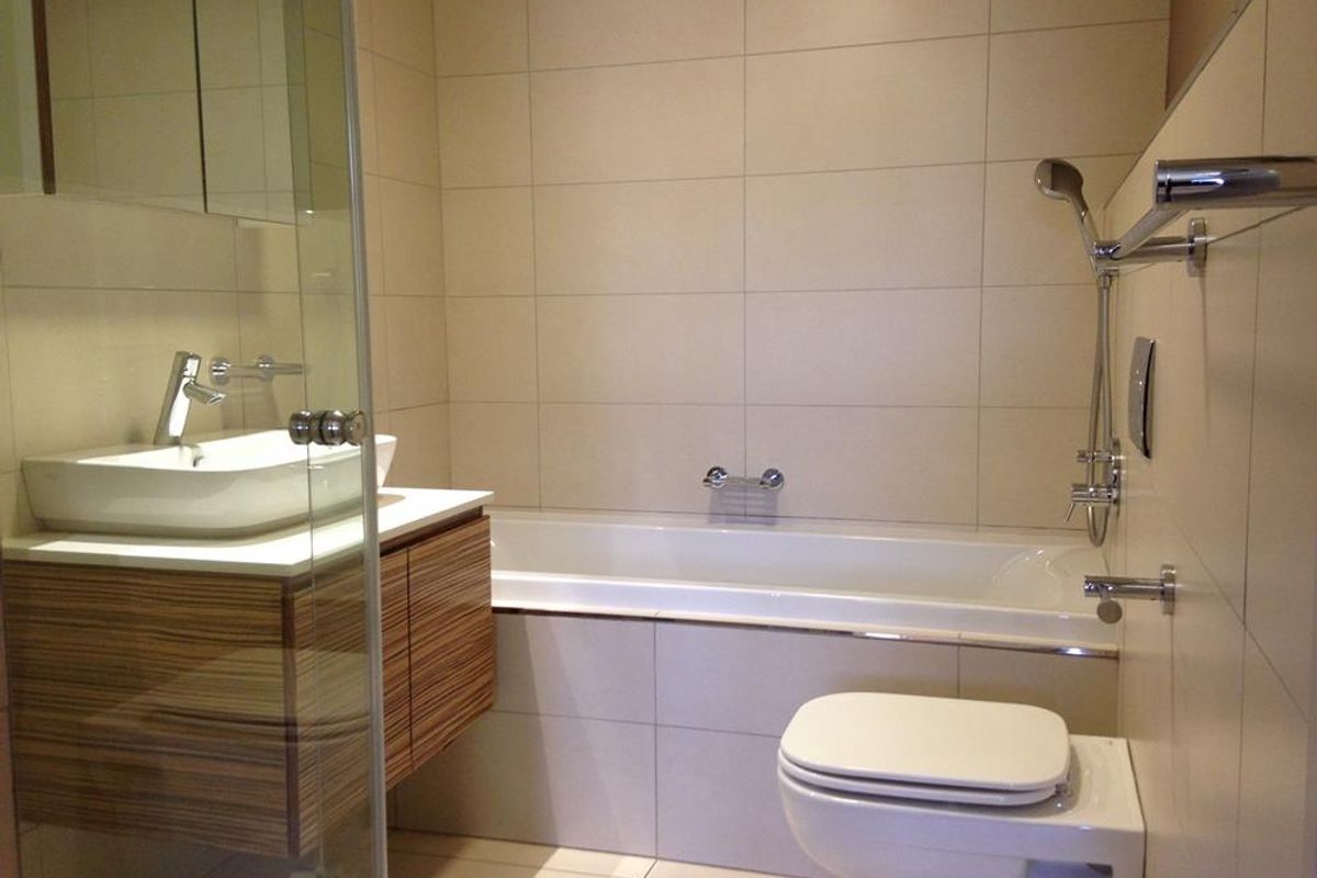 Modern bathroom featuring a wall-mounted vanity with vessel sink, built-in bathtub, wall-hung toilet, and neutral floor-to-ceiling tiling.