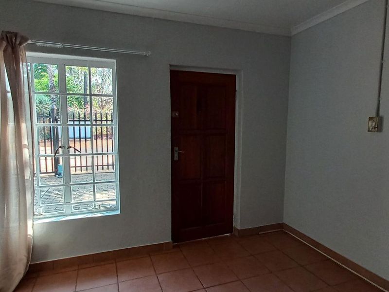 A simple, empty bedroom featuring tiled flooring, a timber door, and a window with security bars, providing a blank canvas for potential updates.