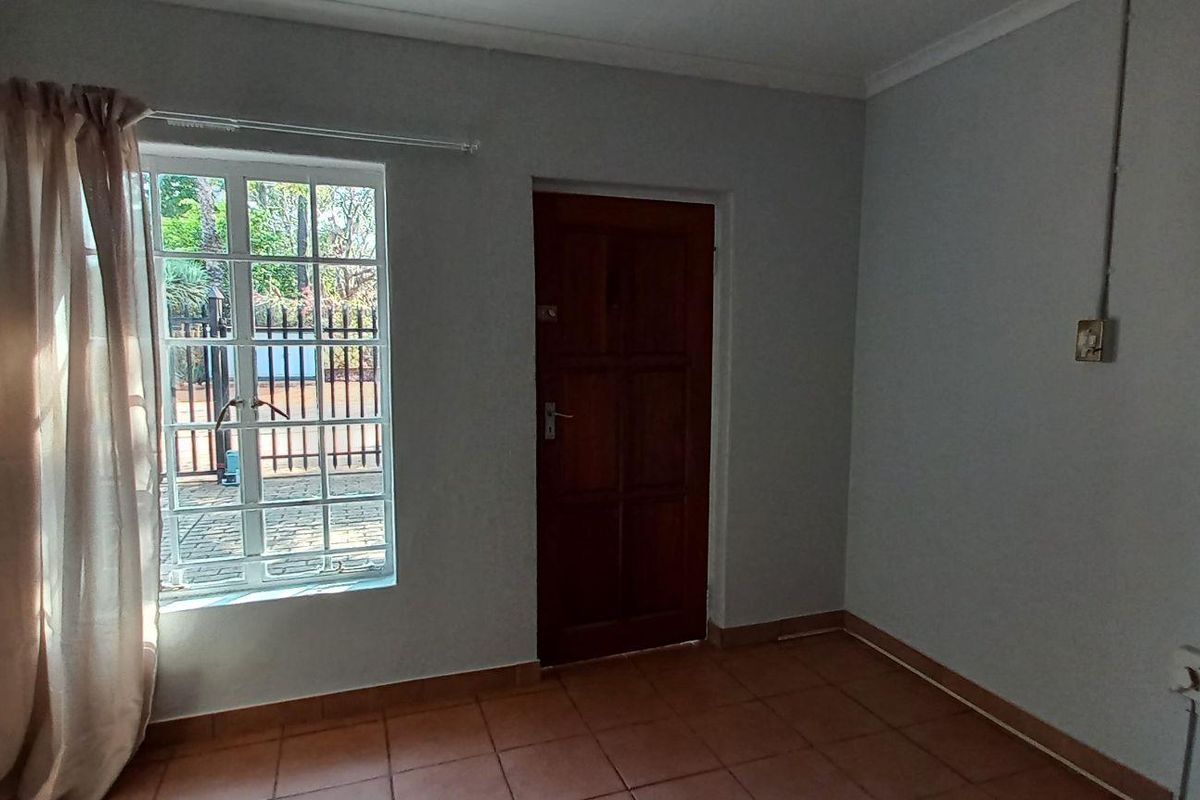 A simple, empty bedroom featuring tiled flooring, a timber door, and a window with security bars, providing a blank canvas for potential updates.