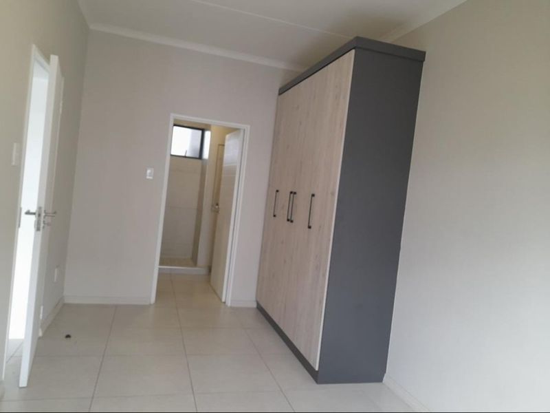 A clean, neutral bedroom featuring modern tiled flooring, a large built-in wardrobe, and direct access to an en-suite bathroom.