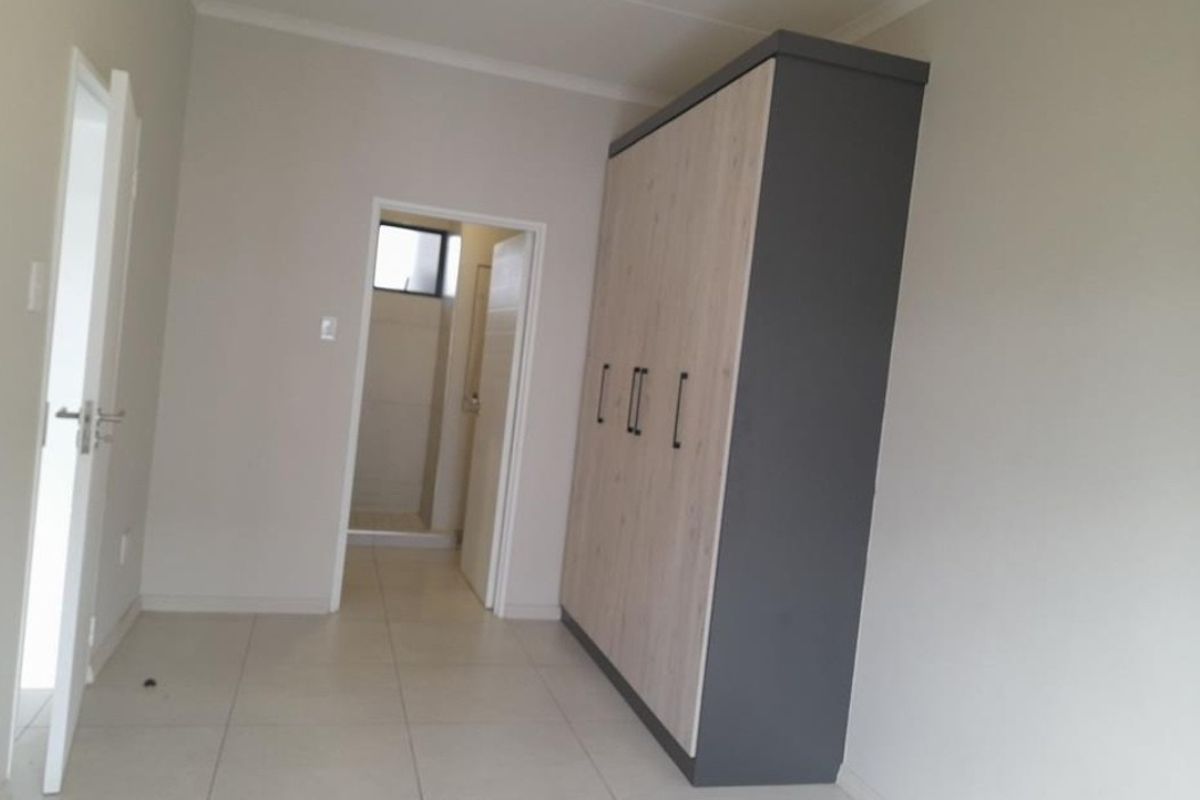 A clean, neutral bedroom featuring modern tiled flooring, a large built-in wardrobe, and direct access to an en-suite bathroom.