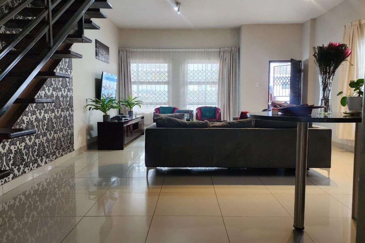 Spacious living room featuring large format floor tiles and an open-plan staircase with decorative wallpaper, leading to a bright lounge area with security features.