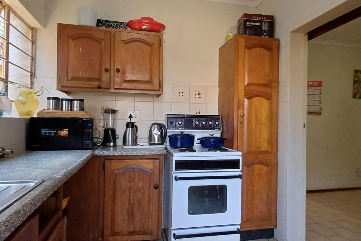 A dated kitchen featuring wooden cabinetry, laminate countertops, a tiled backsplash, and a freestanding electric stove.