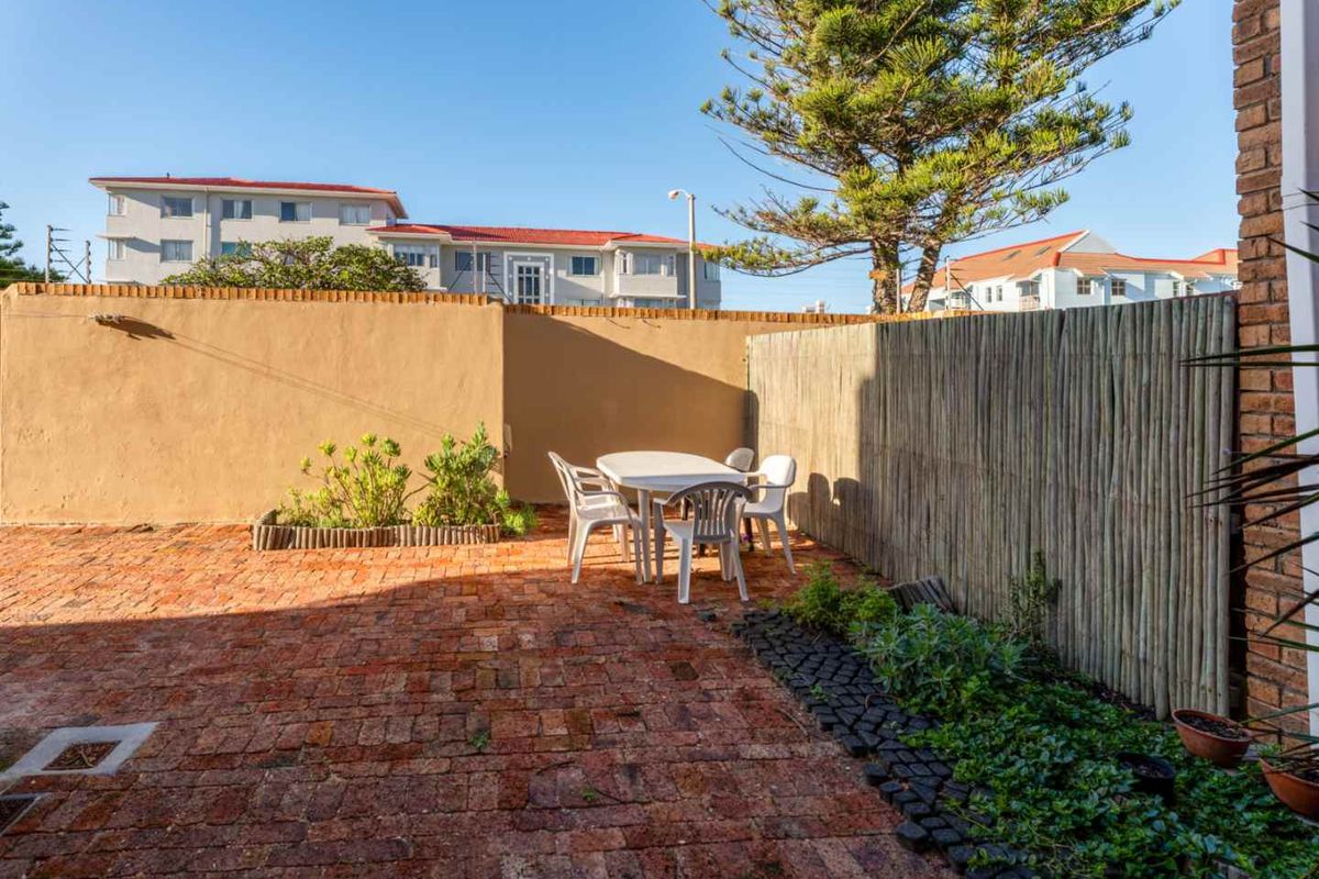 A private rear courtyard featuring brick paving, established garden beds, and a bamboo privacy screen, offering a functional outdoor space.