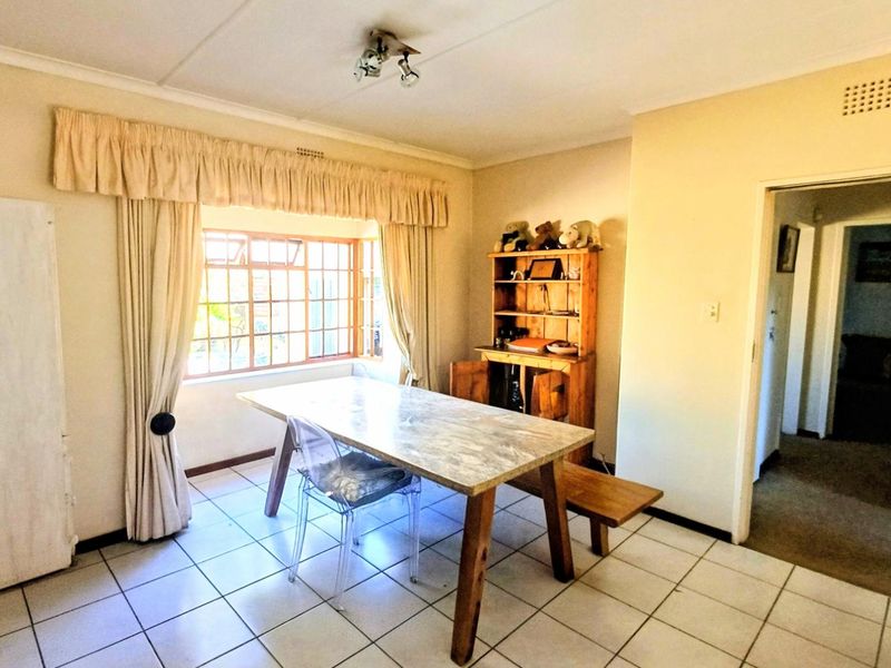 A functional dining area featuring tiled flooring, a large steel-framed window, and neutral wall finishes, providing a bright and practical space for meals.