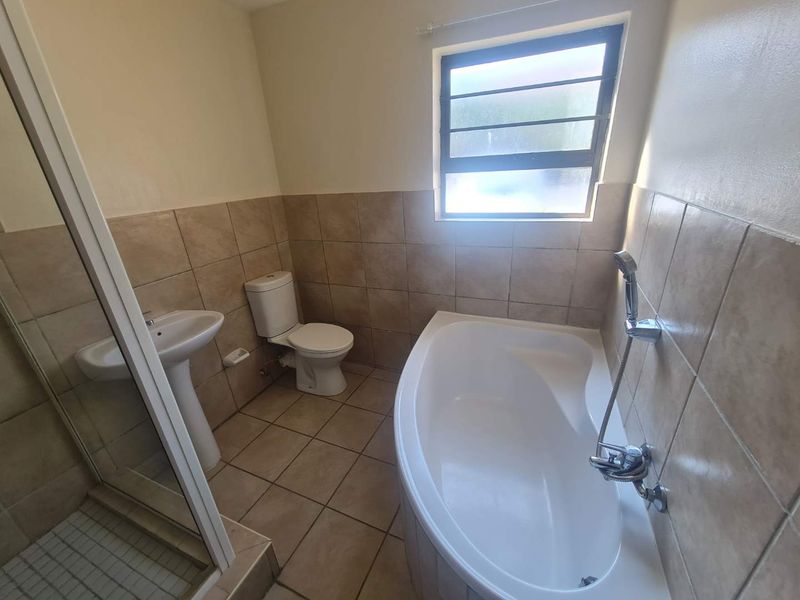 A functional bathroom featuring a corner bathtub, separate shower enclosure, pedestal basin, and toilet with neutral wall and floor tiling.