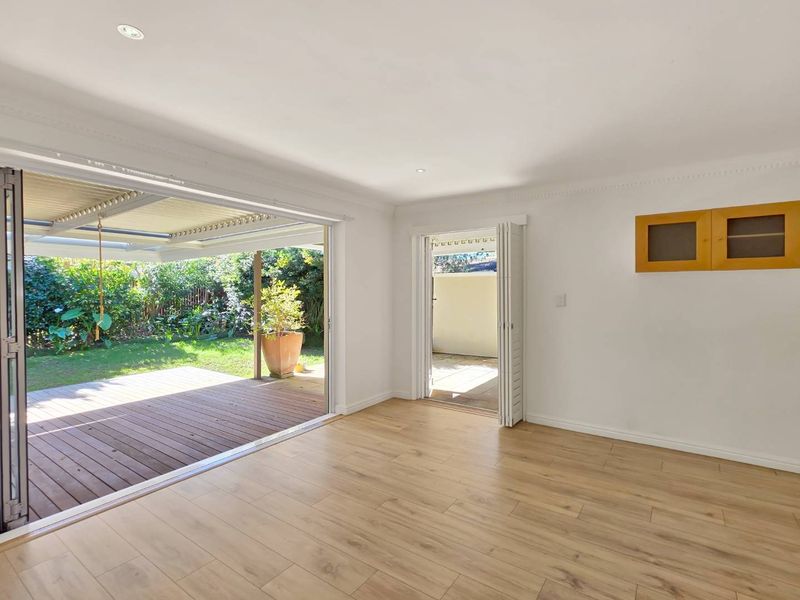 Bright living area featuring laminate flooring, recessed lighting, and seamless indoor-outdoor flow through bi-fold doors to a covered timber deck and garden.