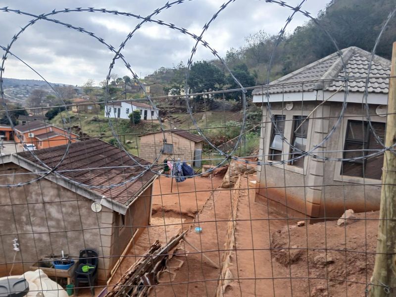 View of the rear exterior area showing multiple structures with tiled roofs, concrete block walls, and security fencing.