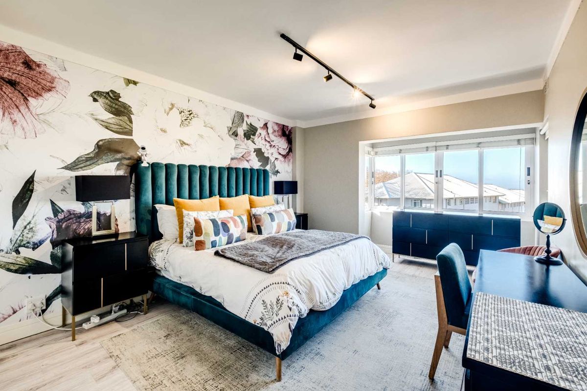 A well-maintained bedroom featuring a floral accent wall, modern track lighting, and large windows providing natural light and neighborhood views.