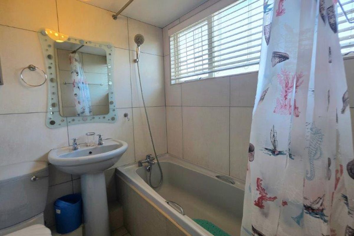 A functional bathroom featuring a pedestal basin, a bathtub with a handheld shower attachment, and neutral wall tiling.