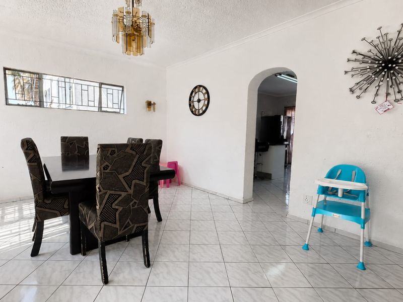A dining room featuring tiled flooring, an arched entryway leading to the kitchen, and classic wall and ceiling lighting fixtures.