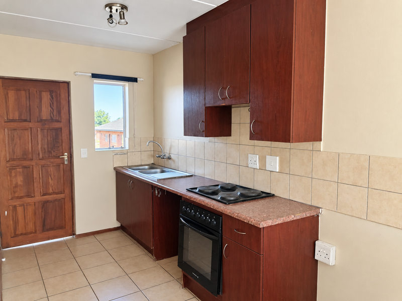 A functional kitchen featuring dark wood cabinetry, a built-in oven with electric hob, tiled backsplash, and neutral floor tiles.